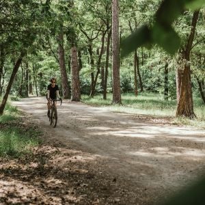 Una mujer hace deporte en bicicleta por un camino en medio de la naturaleza Una mujer hace deporte en bicicleta por un camino en medio de la naturaleza